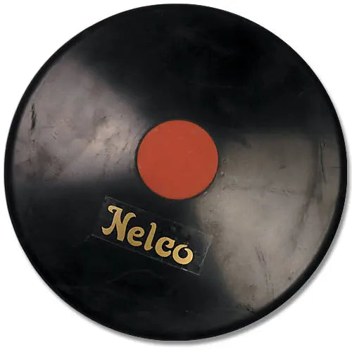 A black Nelco rubber discus with a central orange circular plate, viewed from a direct overhead angle.