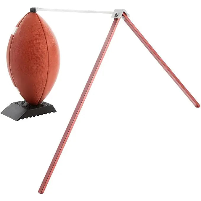 A red, tripod-style Wizard Kicking Stix football holder supporting a brown football on a black base against a white background.