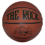A brown leather basketball with black seams, featuring "THE ROCK" text and a city skyline logo with "ROCK 2.0" branding.