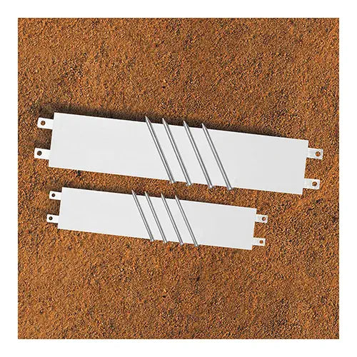 Two white rectangular pitcher's rubbers with attached metal spikes, shown from a top-down angle on a dirt surface.